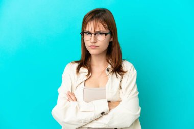 Mavi arka planda gözlüklü ve kolları çaprazlanmış kızıl saçlı bir kız.