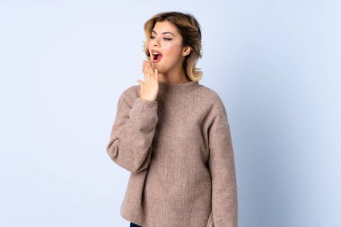 Mavi arka planda izole edilmiş genç bir Rus kadın esniyor ve elleriyle ağzını kapatıyor.