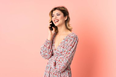 Pembe arka planda izole edilmiş genç bir Rus kadın cep telefonuyla sohbet ediyor.