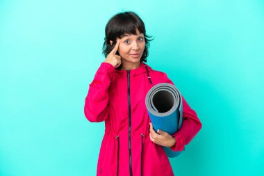 Mavi arka planda bir minder tutarken yoga derslerine giden genç kız bir fikir düşünüyor.