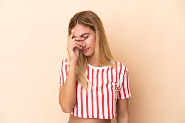 Sarışın Uruguaylı kız bej arka planda baş ağrısı ile izole edilmiş.