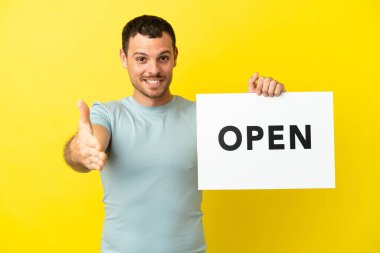 Mor arkaplan üzerinde Brezilyalı bir adam elinde bir pankartla bir anlaşma yapıyor.