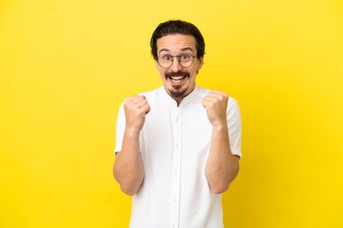 Sarı arka planda izole edilmiş genç beyaz adam galibiyeti kutluyor.