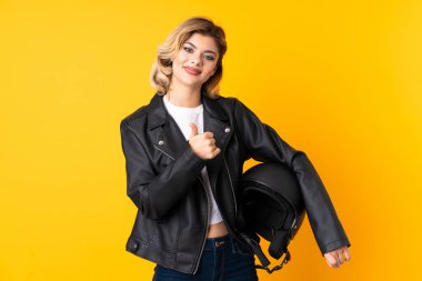 Sarı arka planda izole edilmiş motosiklet kaskı tutan genç bir kadın baş parmak işareti yapıyor.