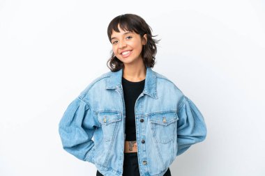 Beyaz arka planda soyutlanmış genç melez bir kadın kolları kalçasında ve gülümsüyor.