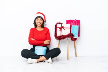 Genç bir kız Noel 'i kutluyor. Beyaz fırında izole bir şekilde yerde oturuyor. Kollarını ön cephede kavuşturuyor.