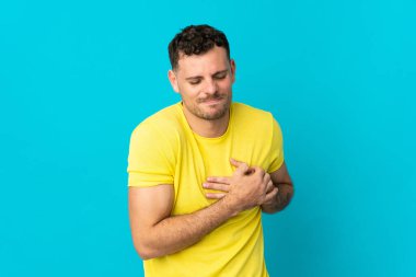 Beyaz tenli yakışıklı bir adam mavi arka planda izole edilmiş, kalbinde ağrı var.