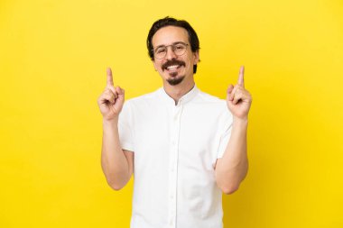 Sarı arka planda izole edilmiş genç beyaz adam harika bir fikre işaret ediyor.