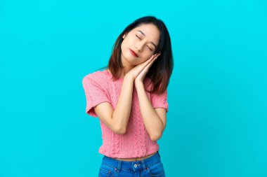 Genç Vietnamlı bir kadın mavi arka planda izole edilmiş bir şekilde uyku jesti yapıyor.