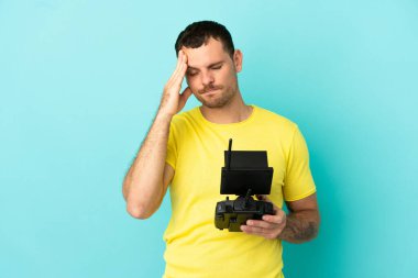 Brezilyalı bir adam uzaktan kumandayla izole edilmiş mavi arkaplanı kontrol ediyor ve başı ağrıyor.