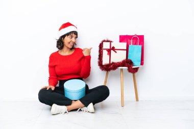 Genç bir kız Noel 'i kutluyor. Beyaz bir fırında izole halde yerde oturuyor. Yan tarafı göstererek bir ürün sunuyor.