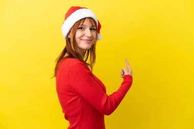 Sarı arka planda izole edilmiş Noel şapkalı kızıl saçlı kız.