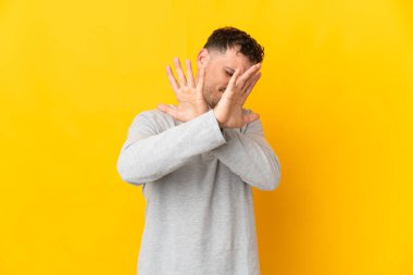 Sarı arka planda izole edilmiş, genç, beyaz, yakışıklı bir adam gergin, ellerini öne uzatıyor.