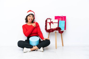 Genç kız Noel 'i kutluyor. Yerde izole bir şekilde oturuyor. Geriye doğru işaret ediyor.