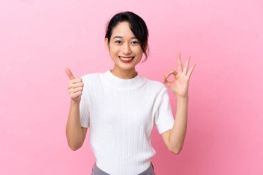 Pembe arka planda izole edilmiş genç Vietnamlı kadın işaret ve baş parmak hareketi gösteriyor.