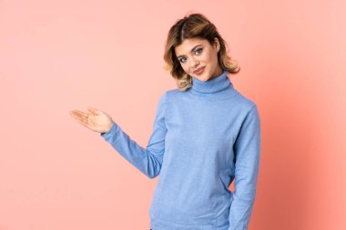 Pembe arka planda izole edilmiş genç bir Rus kadını davet etmek için ellerini yana uzatıyor.