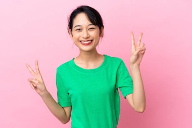 Pembe arka planda izole edilmiş genç Vietnamlı kadın iki eliyle zafer işareti gösteriyor.