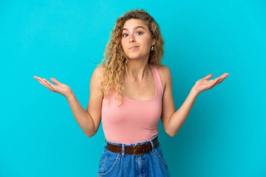 Mavi arka planda izole edilmiş genç sarışın kadın şüpheli hareketler yapıyor.