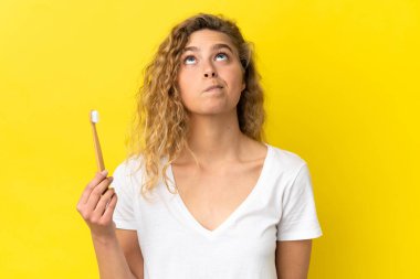 Sarı arka planda dişlerini fırçalayan beyaz bir kadın var.