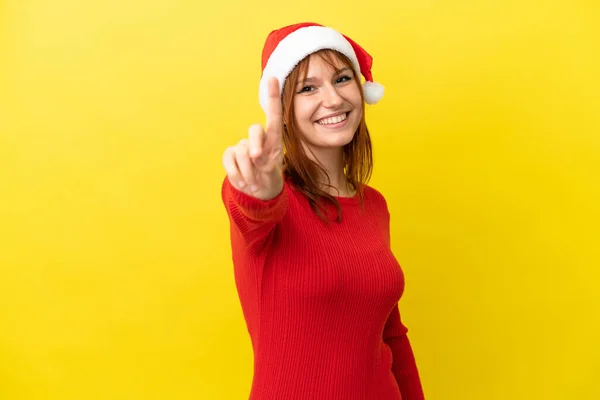 赤毛女の子とともにクリスマス帽子孤立した上に黄色の背景ショーと持ち上げる指 — ストック写真