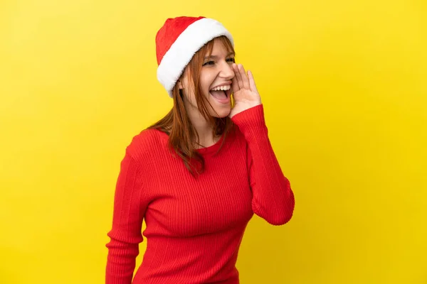 赤毛女の子とともにクリスマス帽子隔離されました上の黄色の背景叫びとともに口を大きく開きますザ側 — ストック写真