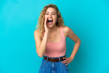 Mavi arka planda izole edilmiş genç sarışın kadın ağzı açık bağırıyor.