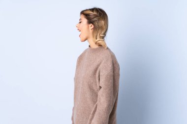 Genç Rus kadın mavi arka planda izole edilmiş. Yan pozisyonda gülüyor.