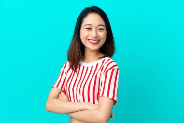 Genç Vietnamlı kadın mavi arka planda izole edilmiş, kolları bağlı ve ileriye bakıyor.