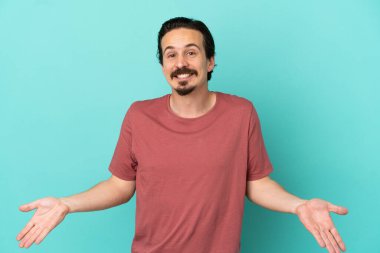 Mavi arka planda izole edilmiş genç beyaz adam mutlu ve gülümsüyor.