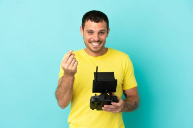 Brezilyalı adam uzaktan kumandayla izole edilmiş mavi arkaplanı kontrol ediyor ve para hareketi yapıyor.