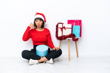 Genç bir kız, Noel 'i beyaz bir fırında izole bir şekilde telefon hareketleriyle yerde oturarak kutluyor. Bana geri dönüş işareti ver.