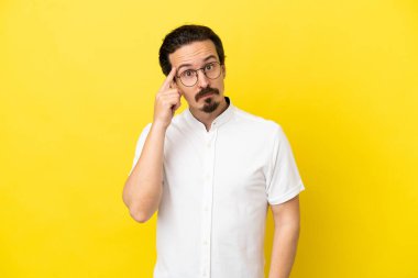 Genç beyaz adam sarı arka planda izole edilmiş bir fikir düşünüyor.
