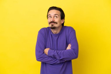 Sarı arka planda izole edilmiş genç beyaz bir adam omuzlarını kaldırırken şüpheyle hareket ediyor.