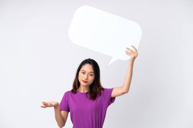 Beyaz arka planda izole edilmiş genç Vietnamlı kadın boş bir konuşma balonu tutuyor ve kuşkuları var.