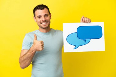 İzole edilmiş mor arkaplan üzerinde Brezilyalı bir adam elinde baş parmağıyla konuşma balonu simgesi olan bir levha tutuyor.