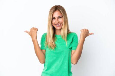 Sarışın Uruguaylı kız beyaz arka planda izole edilmiş. Baş parmakları havada ve gülümsüyor.