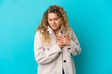 Mavi arka planda izole edilmiş genç sarışın bir kadın. Kalbinde ağrı var.