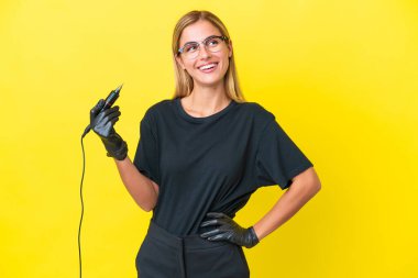 Dövmeci Uruguaylı kadın sarı arka planda izole edilmiş, kolları kalçasında ve gülümsüyor.