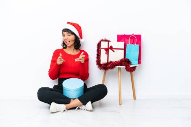 Genç bir kız Noel 'i kutluyor. Yerde izole bir şekilde, beyaz bir fırında oturuyor. Önü gösteriyor ve gülümsüyor.