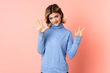 Pembe arka planda izole edilmiş genç Rus kadın parmaklarıyla sekiz sayıyor.