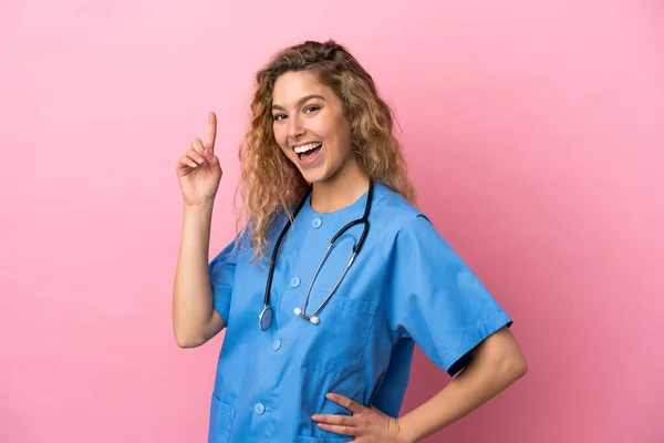 若い外科医の医師の女性はピンクの背景を示すと最高の兆候で指を持ち上げる — ストック写真