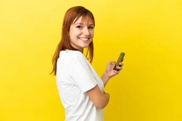 Rotschopfiges Mädchen Isoliert Auf Gelbem Hintergrund Mit Einem Mobiltelefon Und — Stockfoto