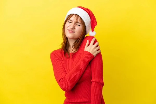 红头发姑娘 头戴一顶黄色背景的圣诞帽 由于付出了巨大的努力 肩头痛苦不堪 — 图库照片