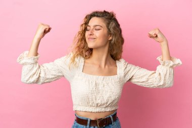 Pembe arka planda izole edilmiş genç sarışın kadın güçlü bir jest yapıyor.