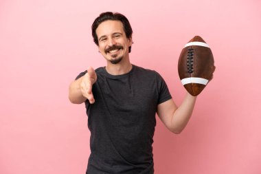 Pembe arka planda izole bir şekilde ragbi oynayan beyaz bir adam iyi bir anlaşma için el sıkışıyor.