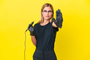 Dövme sanatçısı Uruguaylı kadın sarı arka planda izole edilmiş, dur hareketi yapıyor.