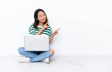 Diz üstü bilgisayarı olan genç Vietnamlı kadın beyaz duvarda izole bir şekilde oturuyor işaret parmağıyla işaret ediyor. Harika bir fikir.