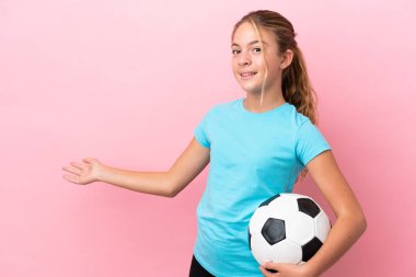 Pembe arka planda izole edilmiş küçük futbolcu kız, davet edilmek için ellerini yana uzatıyor.