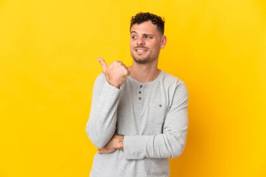Sarı arka planda izole edilmiş beyaz, yakışıklı genç bir adam bir ürün sunmak için kenarı işaret ediyor.
