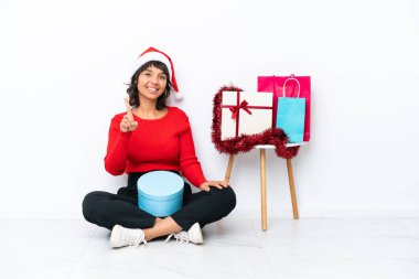 Genç bir kız Noel 'i kutluyor. Beyaz fırında izole bir şekilde yerde oturuyor. Parmağını kaldırıyor ve gösteriyor.